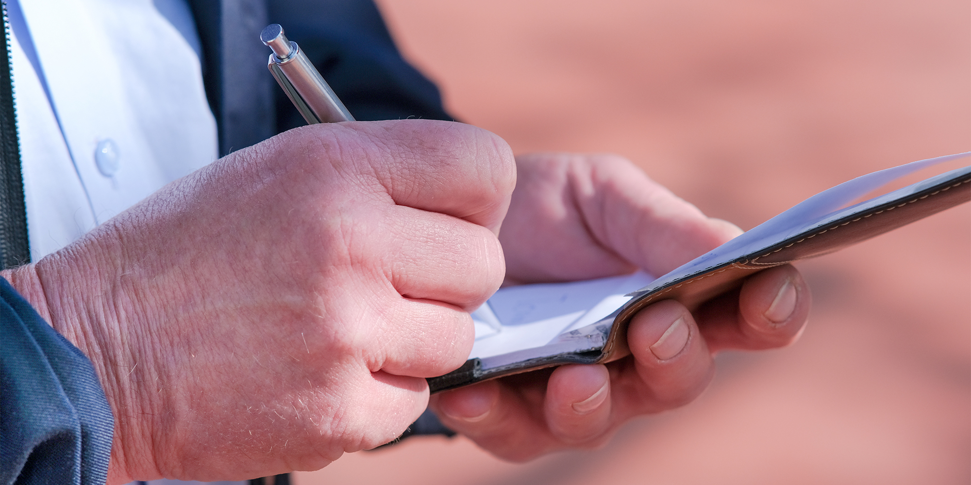 Hands writing with a pen on a pad of paper