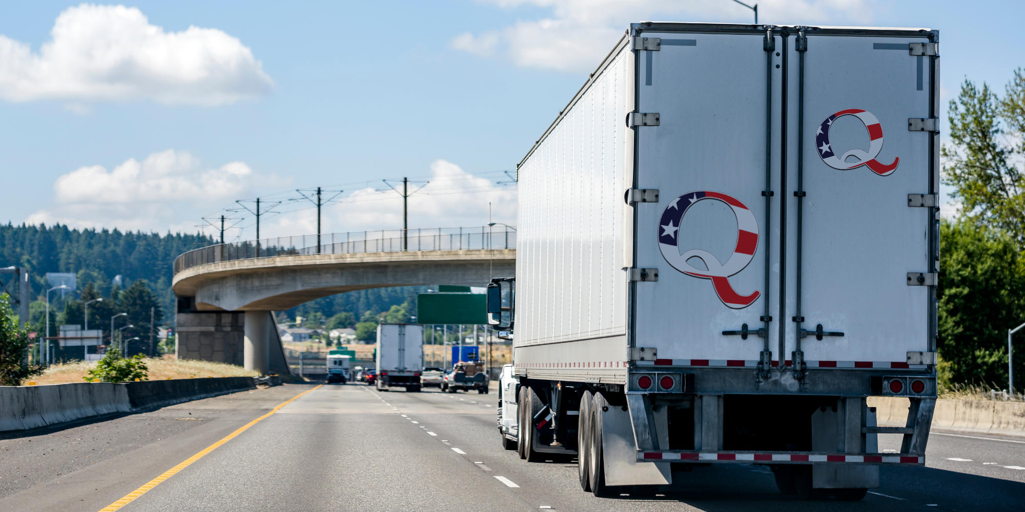 truck driving on road with Qanon stickers on the back