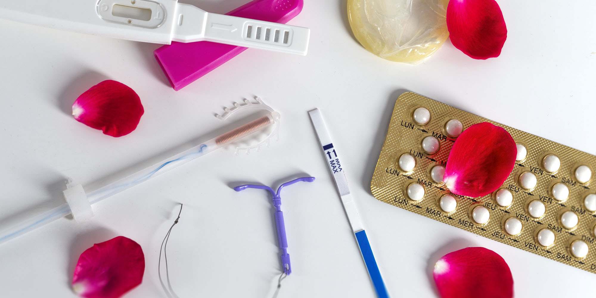 IUD and other various birth control methods on white table with petals scattered