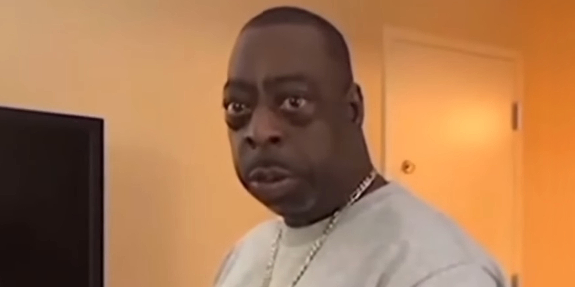 Beetlejuice speaking in front of tan walls and door