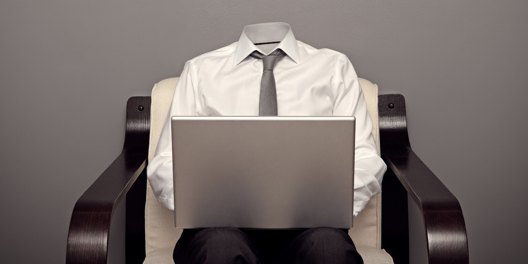 headless business man with laptop in chair in front of grey wall