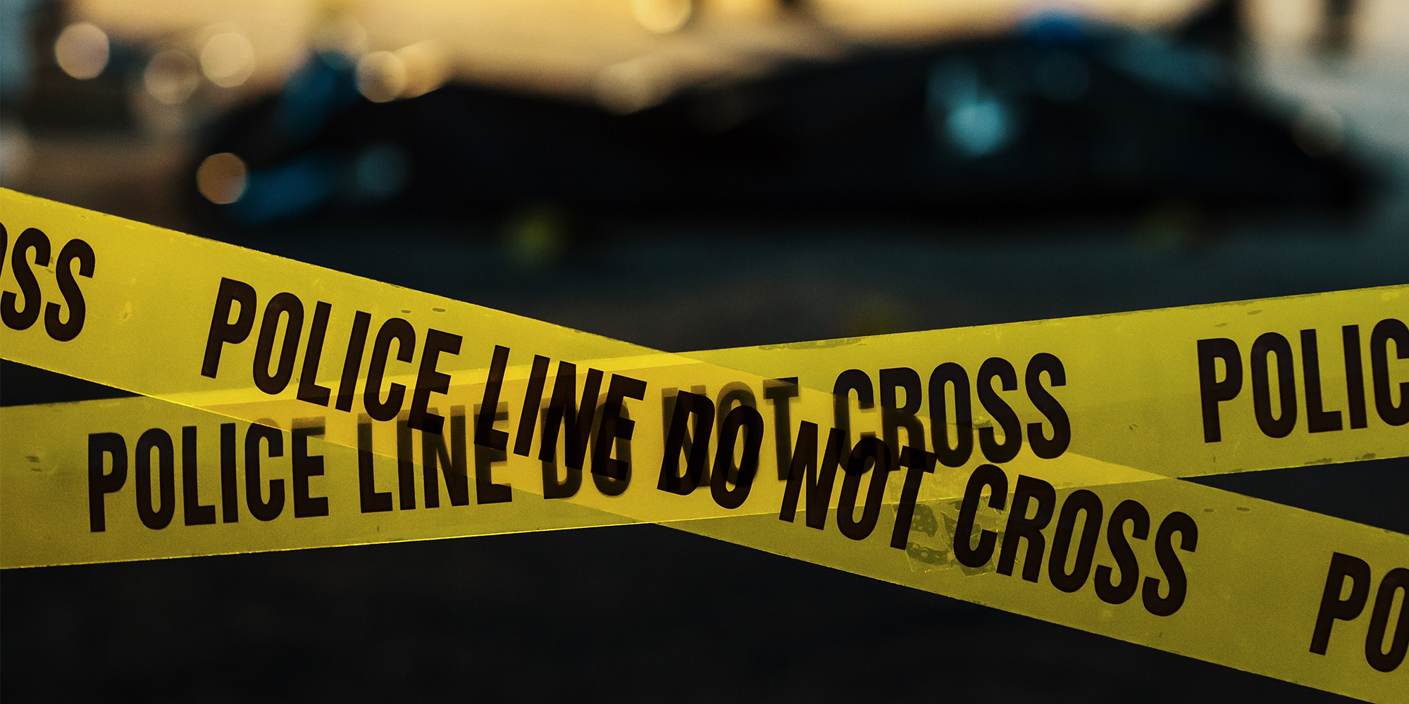 Shot Focused on Yellow Tape Showing Text "Police Line Do Not Cross". Tape Used to Restrict a Crime Scene Where Forensics, Detectives and Policemen are Working on Solving a Homicide Case