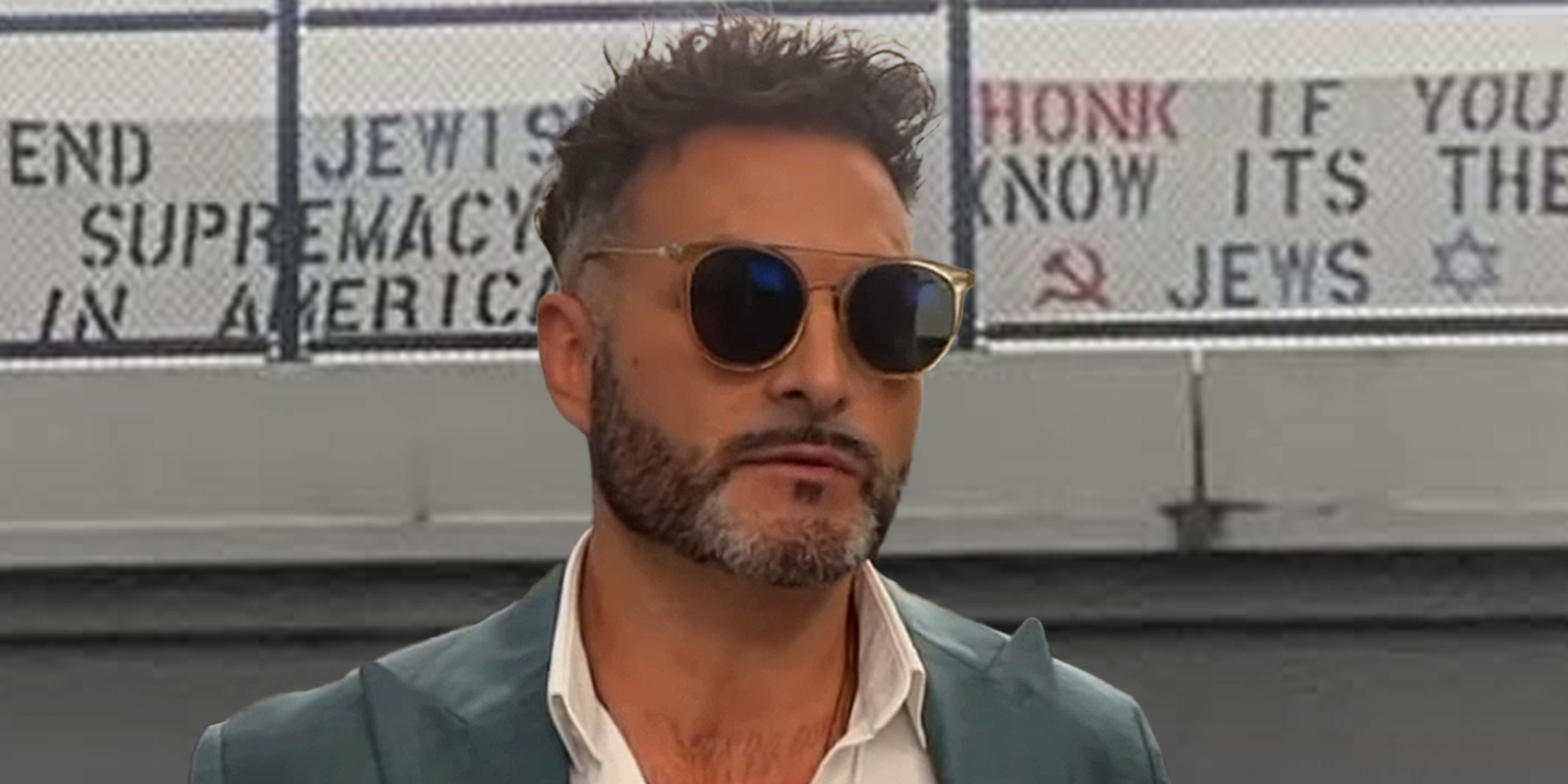 John Minadeo in front of signs hung on highway that read "end Jewish supremacy in America" and "Honk if you know its the Jews"