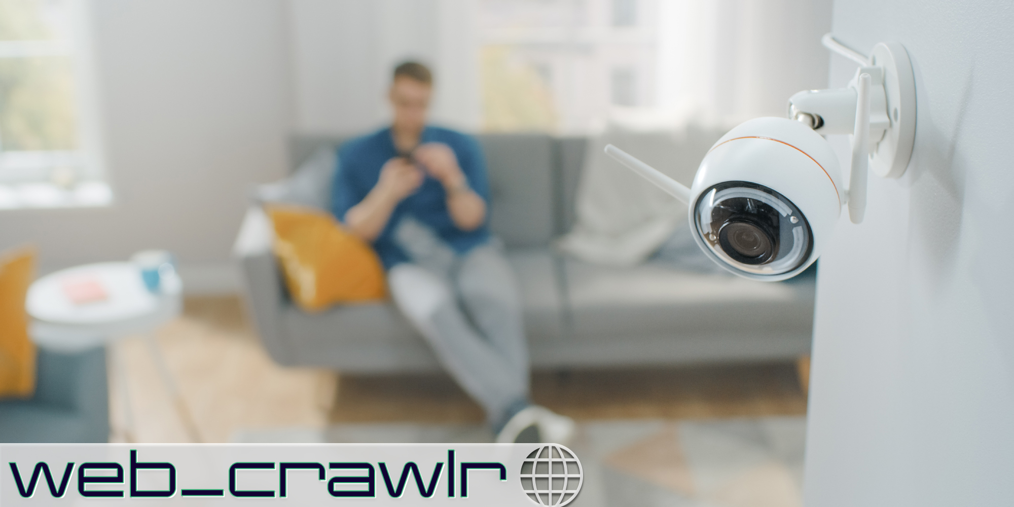 A person sitting on a couch in an apartment with a camera on the wall. The Daily Dot newsletter web_crawlr logo is in the bottom left corner.