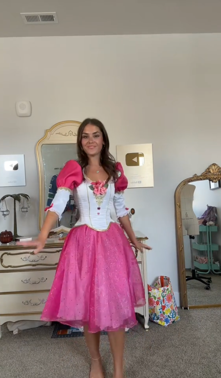 Screenshot of a woman in an ornate pink and white Barbie dress.