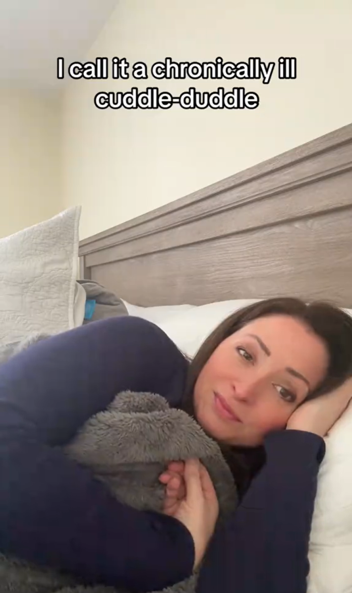 Weary looking woman lying in bed. Text overlay, referencing the "hurkle durkle" meme trend, reads, "I call it a chronically ill cuddle-duddle."