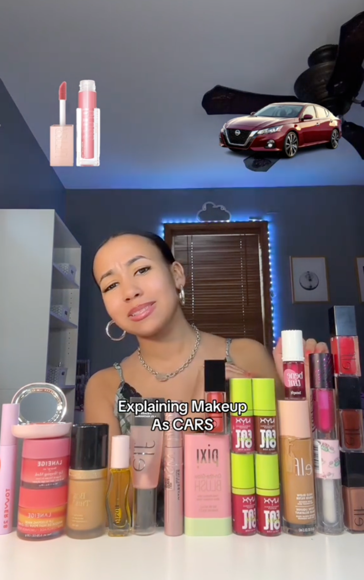 Screenshot of a woman surrounded by makeup products with a photo of a car in the upper right. Text overlay reads, "Explaining Makeup As CARS."