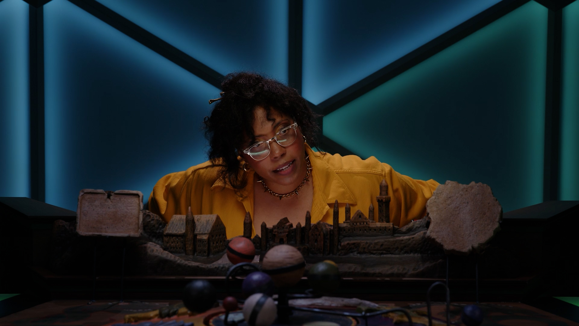 Aabria Iyengar, the Game Master of Dimension 20's show Misfits and Magic, leans over the table in the D20 dome.