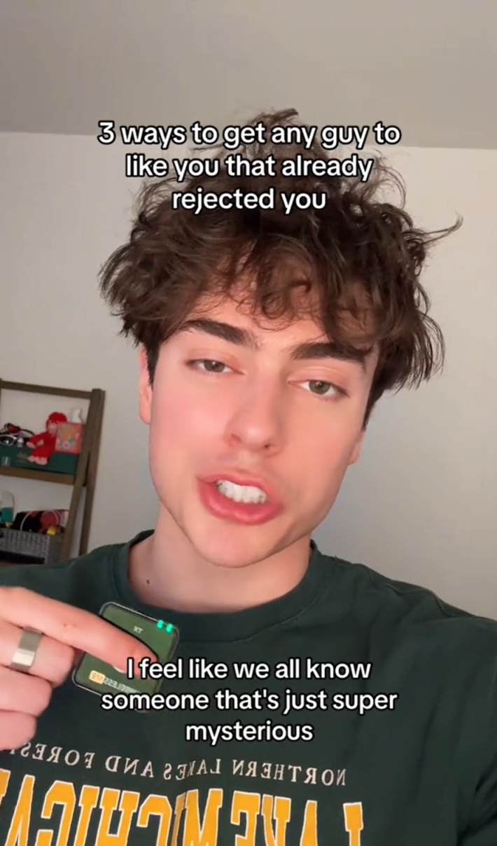 A man with messy hair is talking into the camera while holding a lapel mic in his hand. Text overlay reads, "3 ways to get any guy to like you that already rejected you." A second text box reads, "I feel like we all know someone that's just super mysterious."