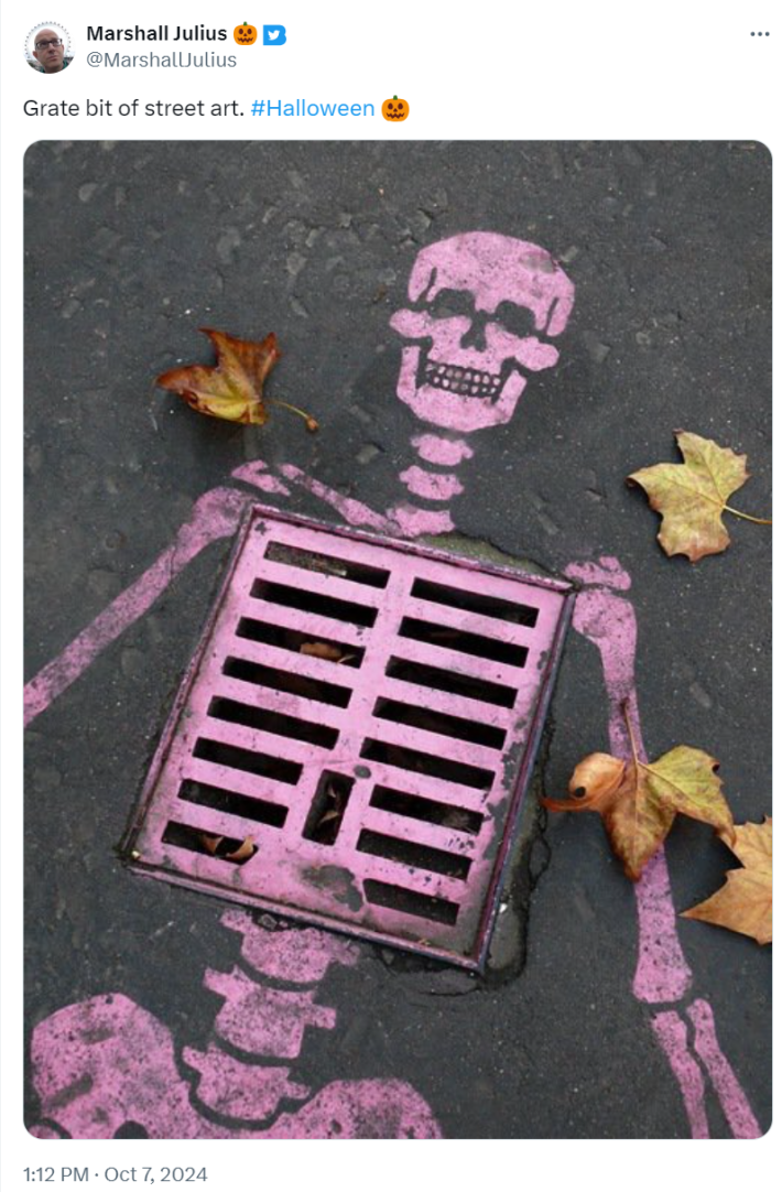 Photo of a spray painted pink skeleton over a grate on the road. Text reads, "Grate bit of street art."
