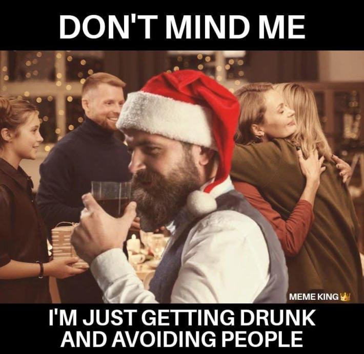 Introvert meme of a guy in a santa hat drinking at an event. Text reads, "Don't mind me, I'm just getting drunk and avoiding people."