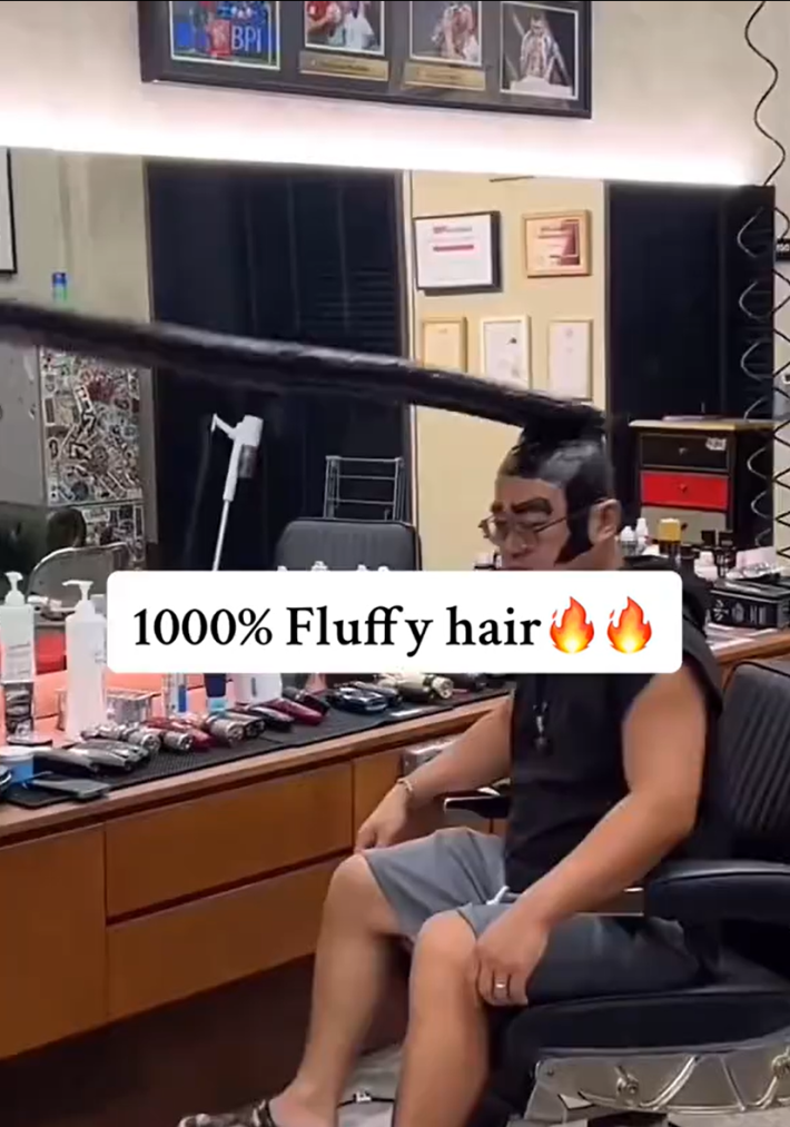 Sigma Sigma Boy trend with text overlay that reads, "1000% Fluffy hair (fire emojis)" with a man sitting in a barber's chair with what looks like black taped hair jutting out four feet in front of him.