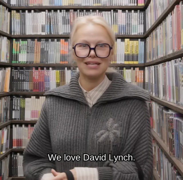 David Lynch meme, text reads, "We love David Lynch." with a woman in large glasses standing in front of shelves of DVDs.