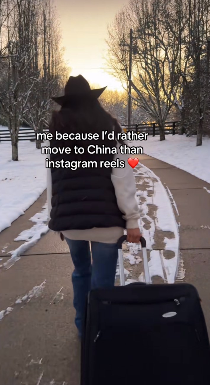 TikTok screenshot of a woman in a cowboy hat walking down her driveway with a big suitcase. Text overlay reads, "me because I'd rather move to China than instagram reels (heart emoji)"