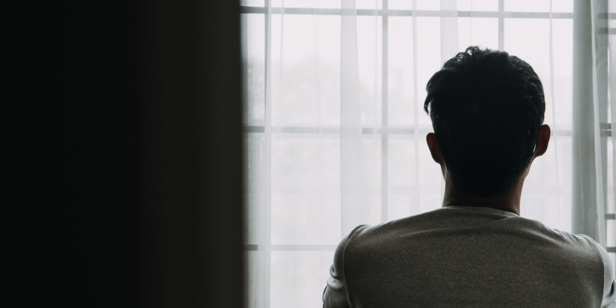 A person sitting in a dark room looking out the window.