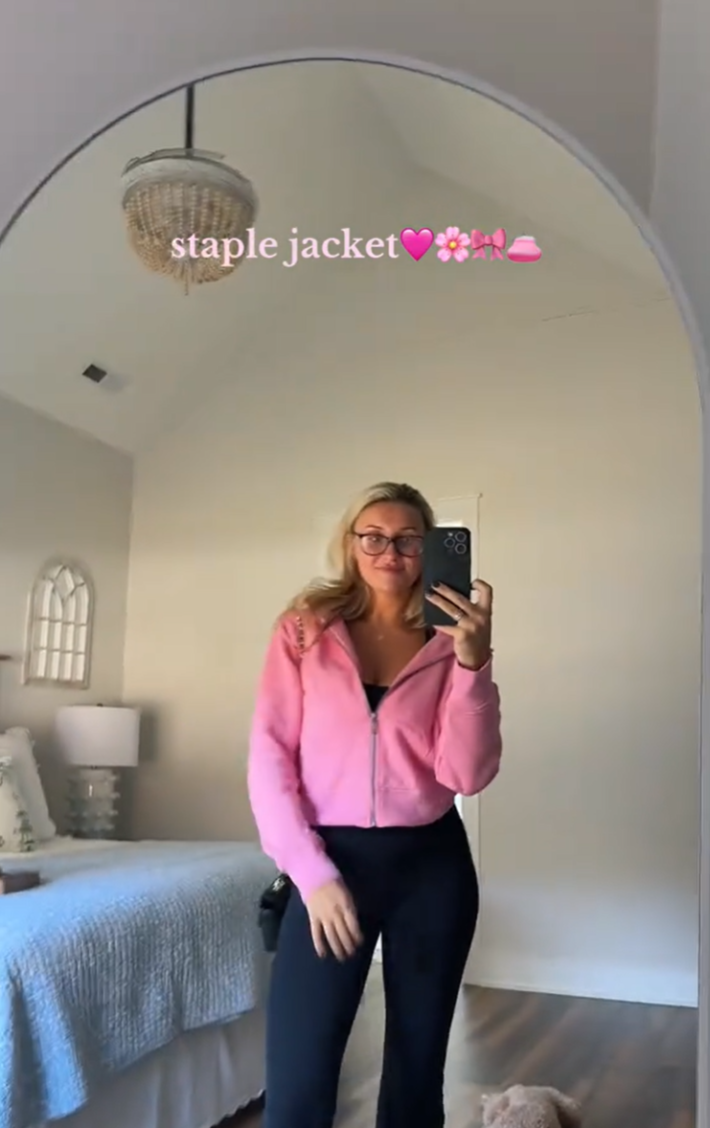 A blonde woman in a pink dupe Scuba hoodie posing for her camera.