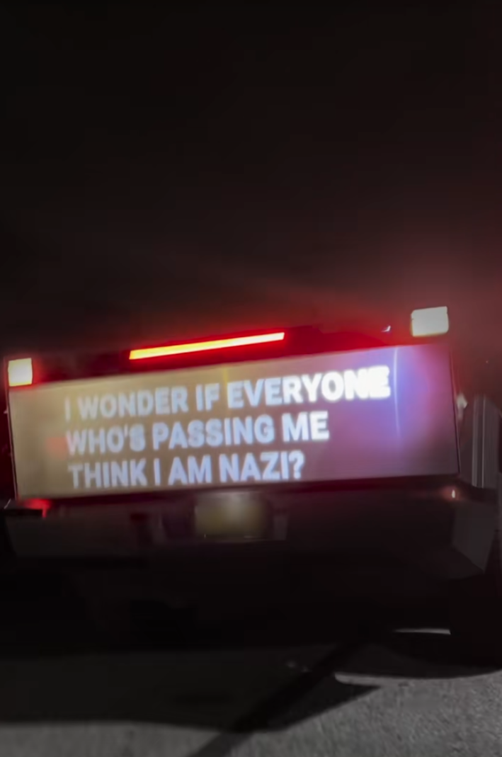 Cybertruck with a projection on it that reads, "I wonder if everyone who's passing me think I am Nazi?"