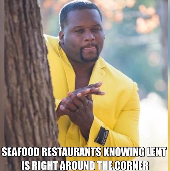 Lent meme, text reads, "Seafood restaurants knowing Lent is right around the corner." with a man in a yellow suit rubbing his hands together behind a tree.