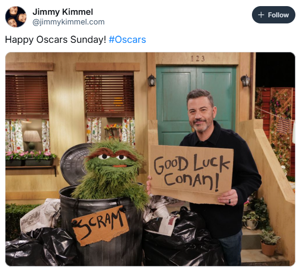 Oscars meme from Jimmy Kimmel, text reads, "Happy Oscars Sunday!" with a photo of him standing next to Oscar the Grouch in his trash can. They are holding cardboard signs that say "SCRAM" (Oscar) and "Good luck Conan!" (Kimmel)