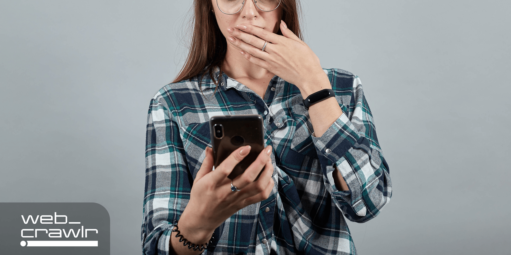 A person looking at an iPhone with her hand over her mouth. The Daily Dot newsletter web_crawlr logo is in the top left corner.