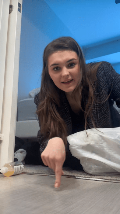 Screenshot of a woman on the floor putting stuff in a trash bag pointing with her finger to make a point.