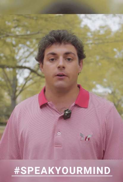 A man in a pink polo shirt speaking to the camera over the hashtag #SPEAKYOURMIND.