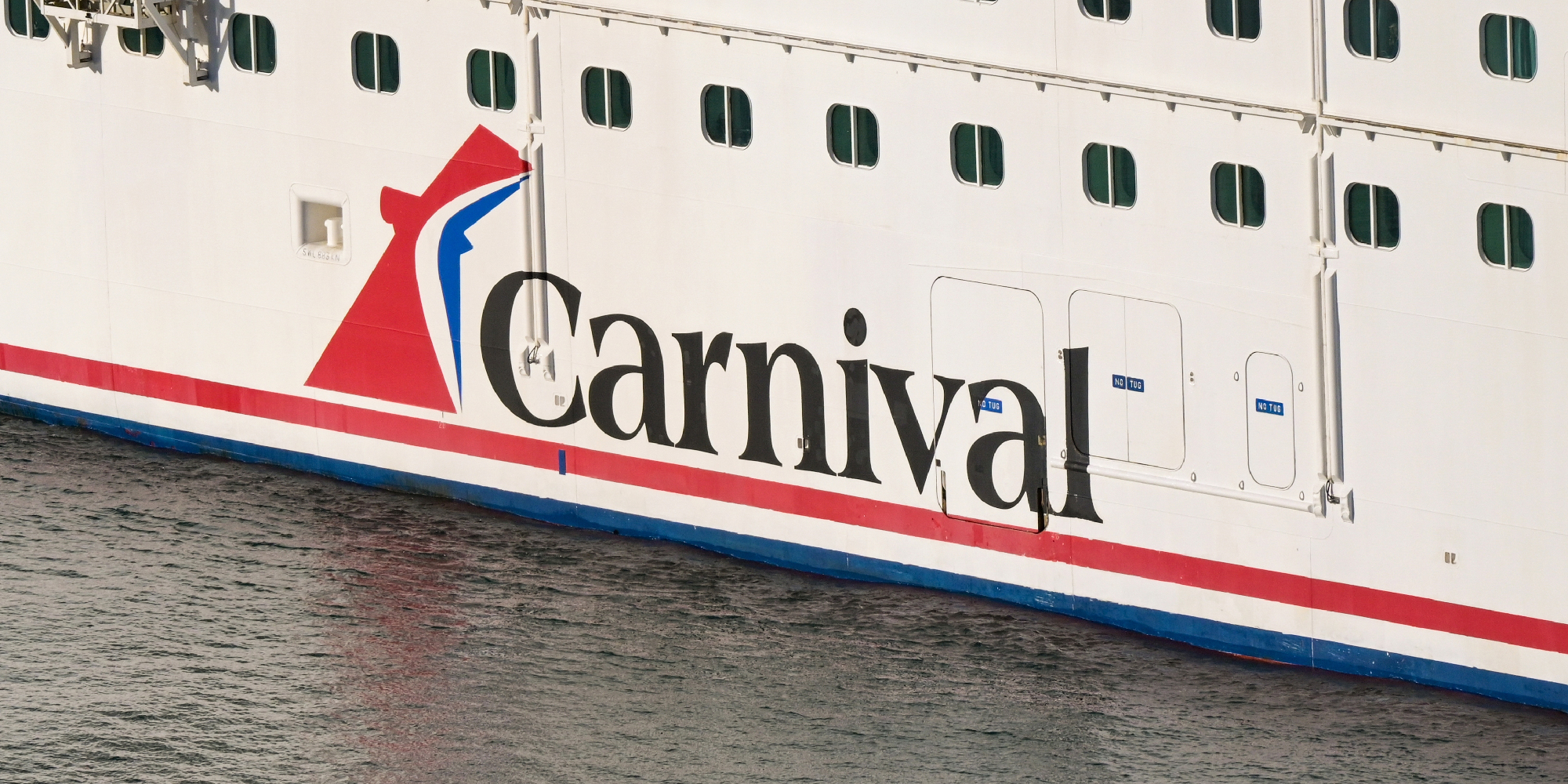 Photo of a Carnival brand cruise ship reflected in water.
