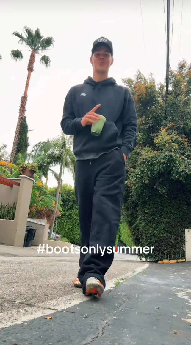 Noah Beck in a parking lot showing off his soccer cleats.