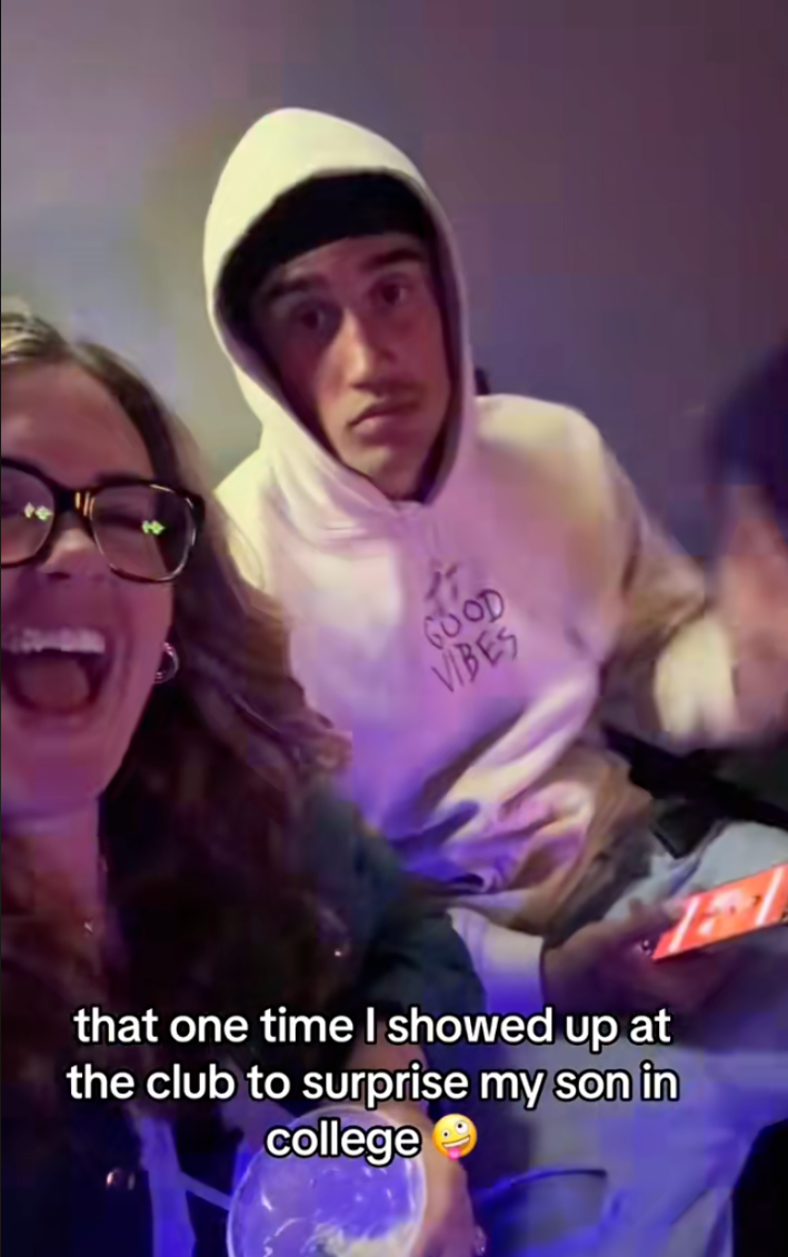 Boy mom singing and drinking while her college son plays on his phone at the bar.