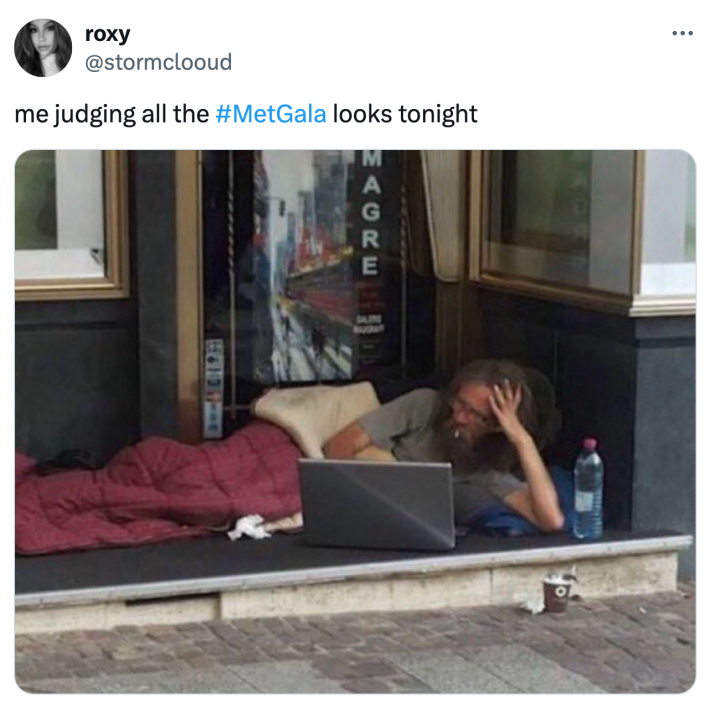 Tweet that says, "me judging all the #Met Gala looks tonight" with a photo of an unhoused man smoking a cigarette and on a laptop.