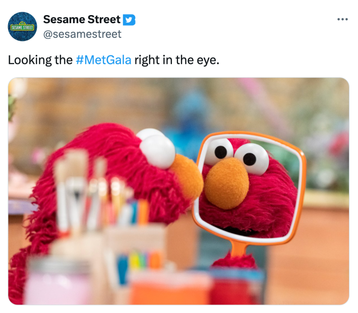 Tweet from Sesame Street that says, "Looking the #MetGala right in the eye." with a photo of Elmo looking at the camera through a hand mirror.