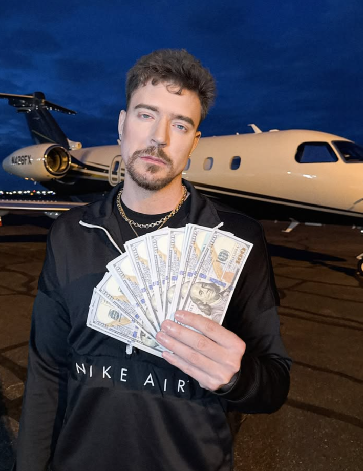 MrBeast holding up a stack of cash in front of a private jet, looking zoned out.