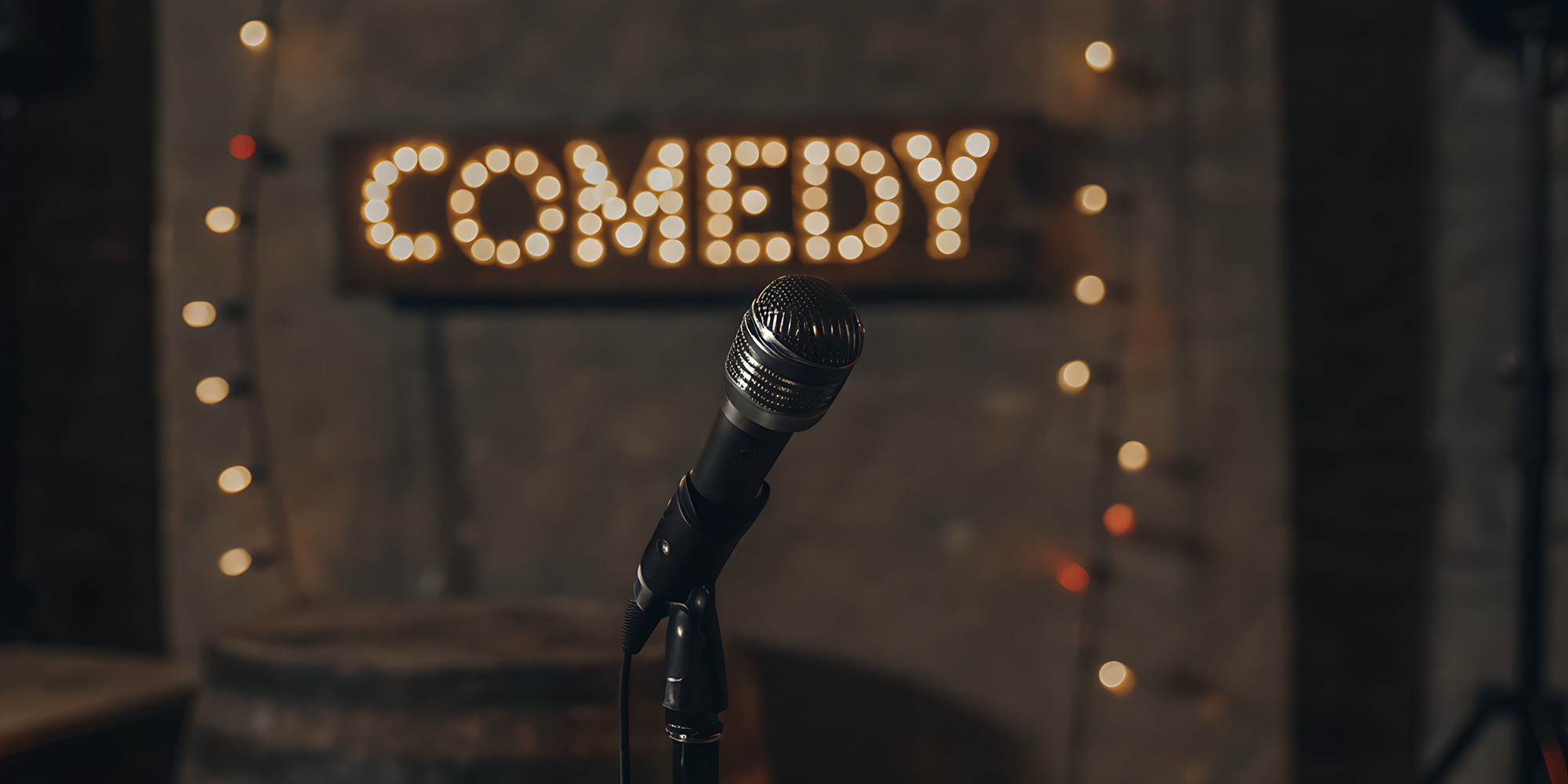 A stand up microphone and stool sit on an empty stage.
