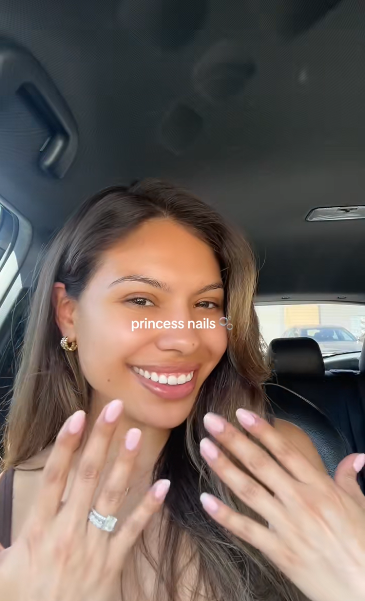A woman in a car showing off her light pink nails, or "princess nails."