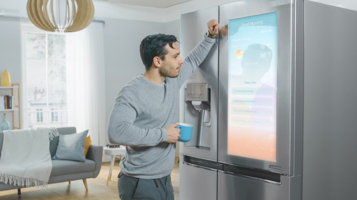 Handsome Young Man is Standing Next to a Refrigerator While Drinking His Morning Coffee