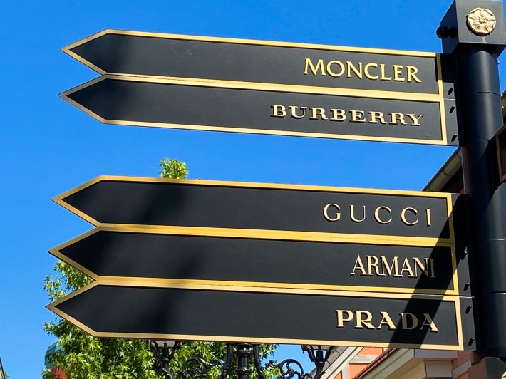 Roermond, Netherlands - May 19. 2020: View on direction arrows with luxury fashion brands against blue sky