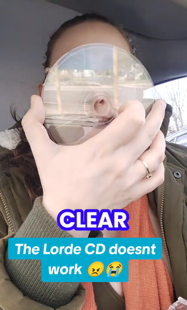 Woman in a care holding up a clear CD for the camera. Text overlay says, "The Lorde CD doesn't work"