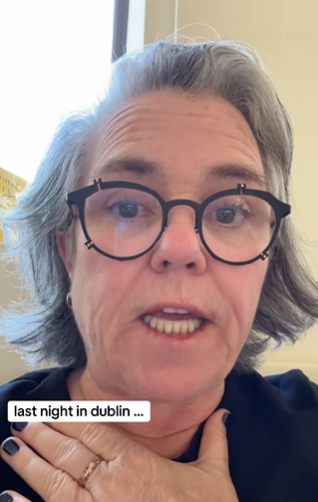 Rosie O'Donnell showing the international sign for choking, one hand clutching her throat.