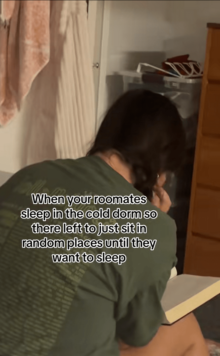 A sorority college student sitting on the floor reading a book. Text overlay reads, "When your roommates sleep in the cold dorm so [they're] left to just sit in random places until they want to sleep."
