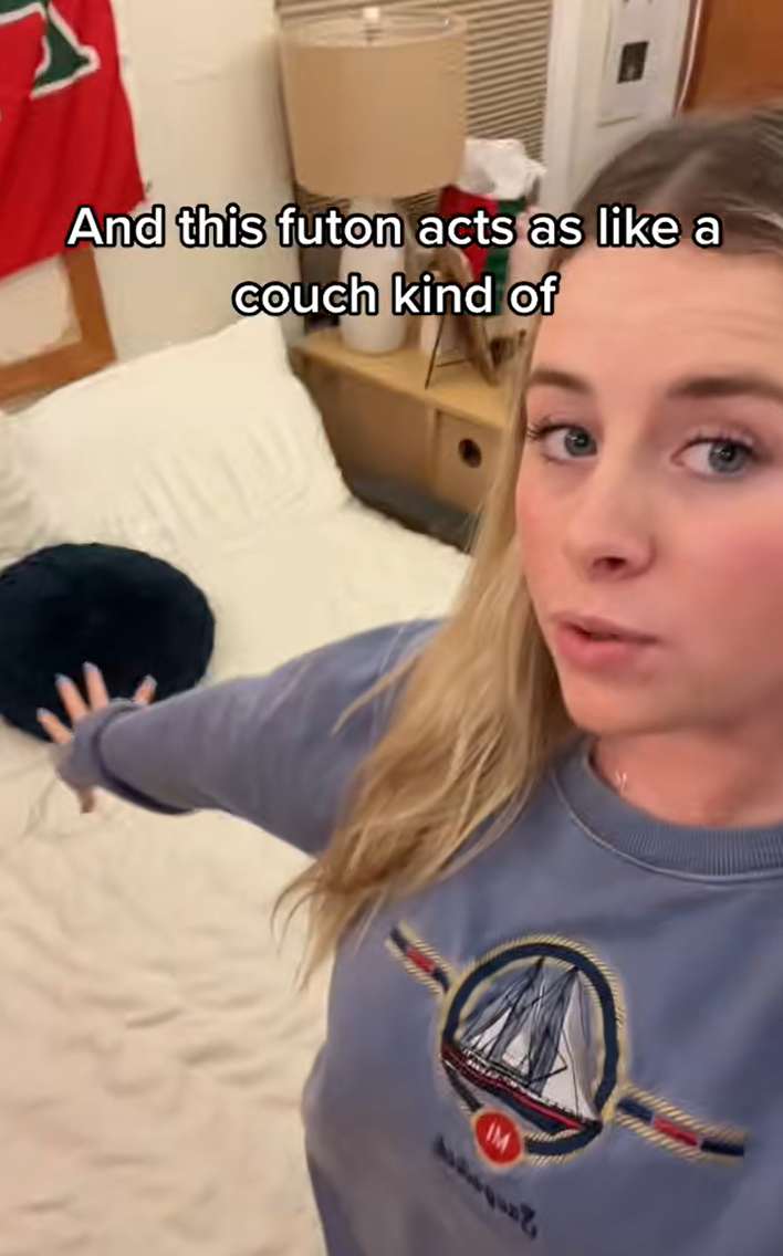 Sorority college student showing off her "day room." Text overlay reads, "And this futon acts as like a couch kind of."