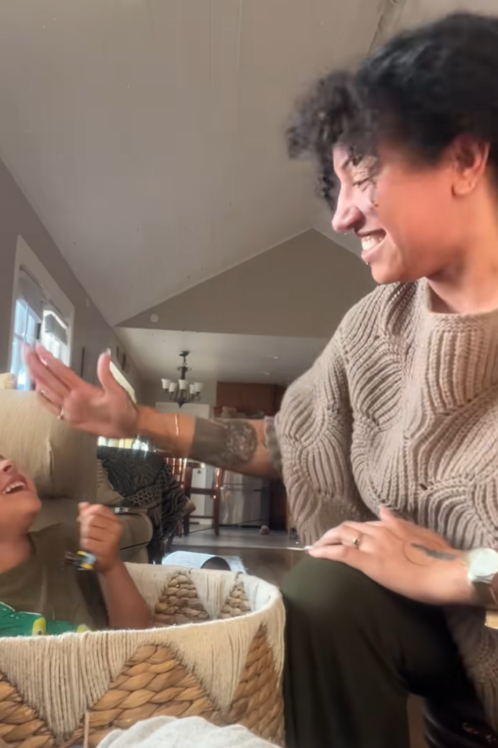 A woman smiling with her raised hand in a playful, mock-slap motion toward her toddler, who is giggling.