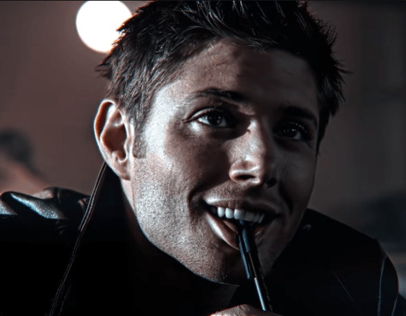 Dean from Supernatural grinning devilishly while biting a pen.