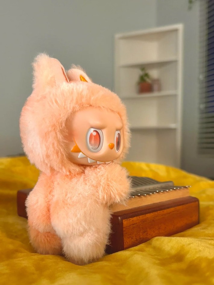 A peach Labubu with a BBL looking cheekily over its shoulder.