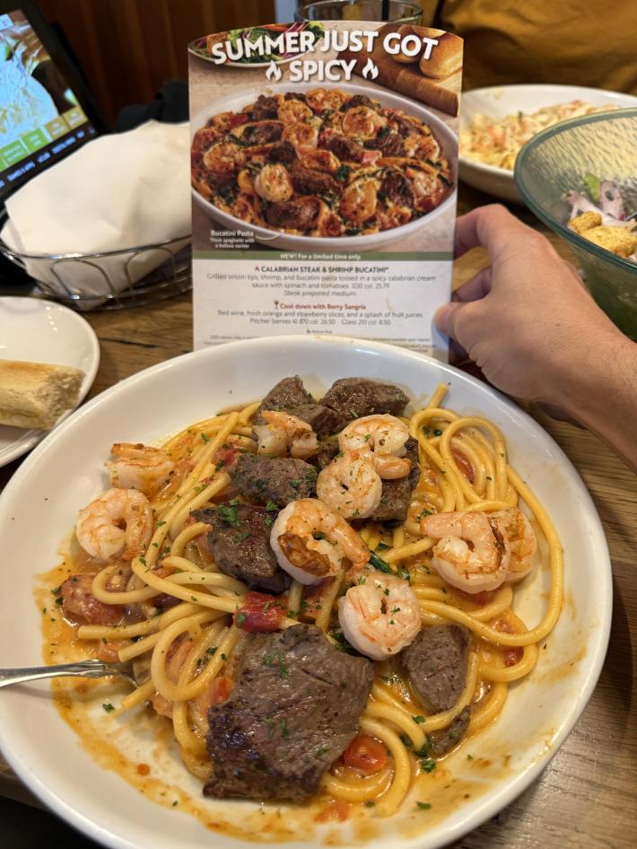 Photo of an Olive Garden ad for steak and shrimp bucatini next to the real thing.