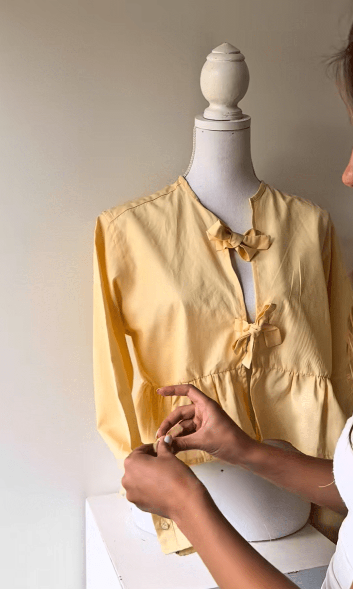 Woman adding bows to a butter yellow top she thrift flipped.