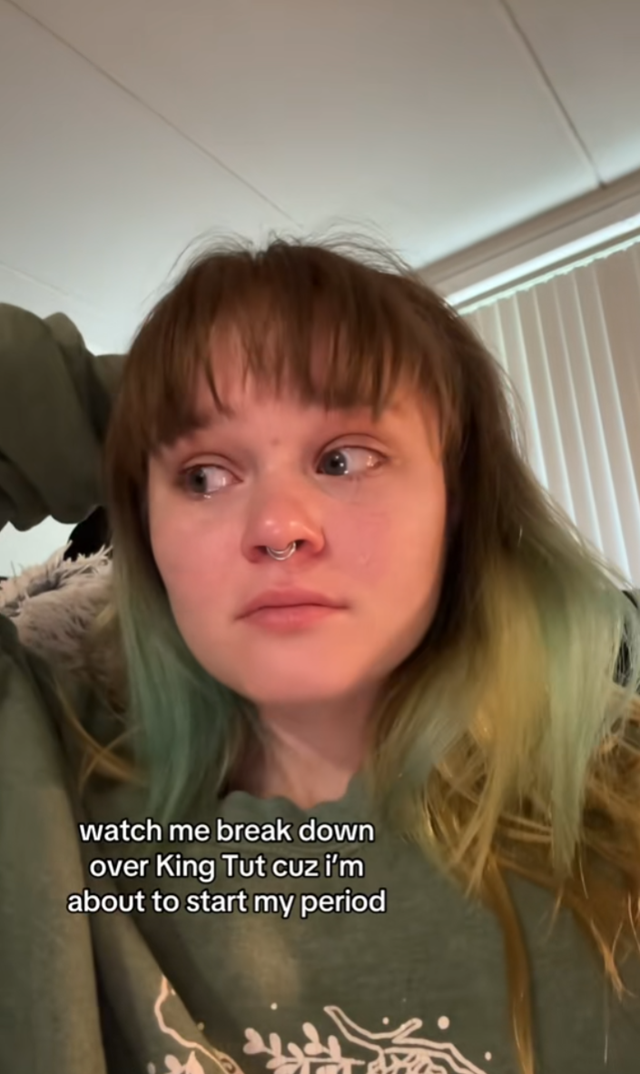 A person with dyed green hair tearfully talking about King Tut. Text overlay reads, "Watch me break down over King Tut cuz I'm about to start my period."