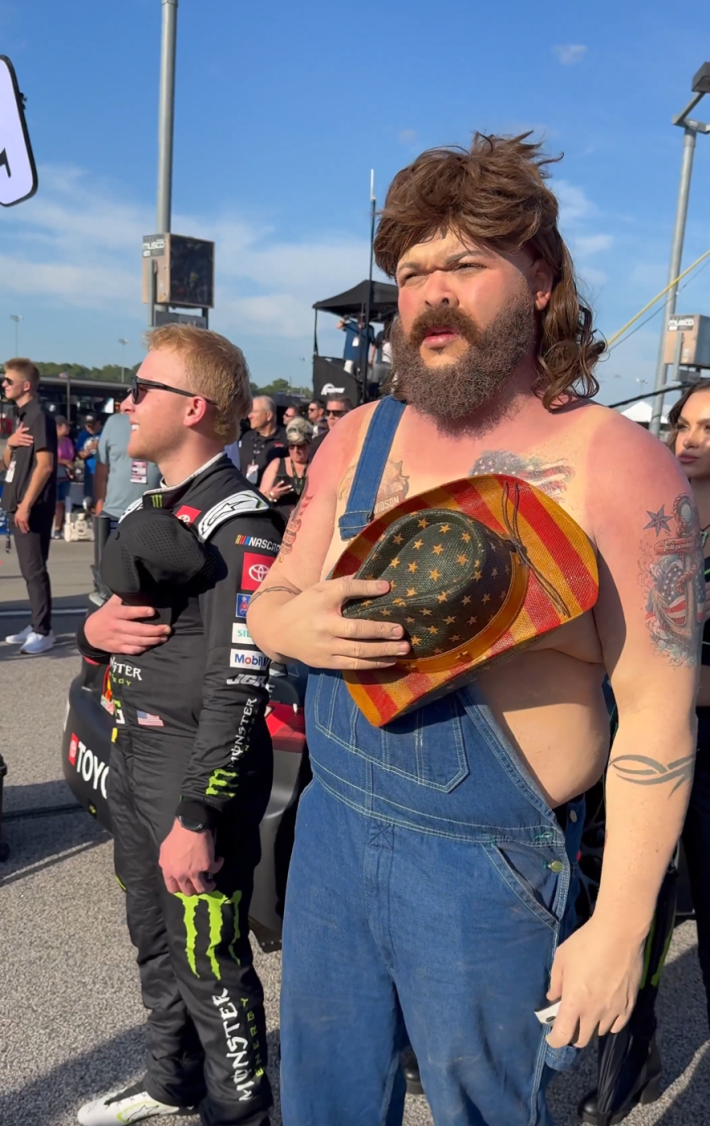Druski holding an American flag cowboy hat to his chest during the national anthem.