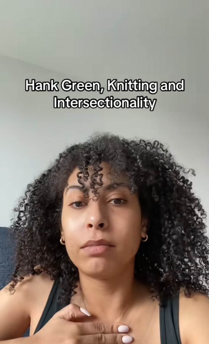 A woman with her hand pressed to her chest. Text overlay reads, "Hank Green, Knitting and Intersectionality."