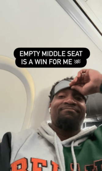 The man filming the encounter pulling his eye mask down with a smile. Text overlay reads, "Empty middle seat is a win for me."