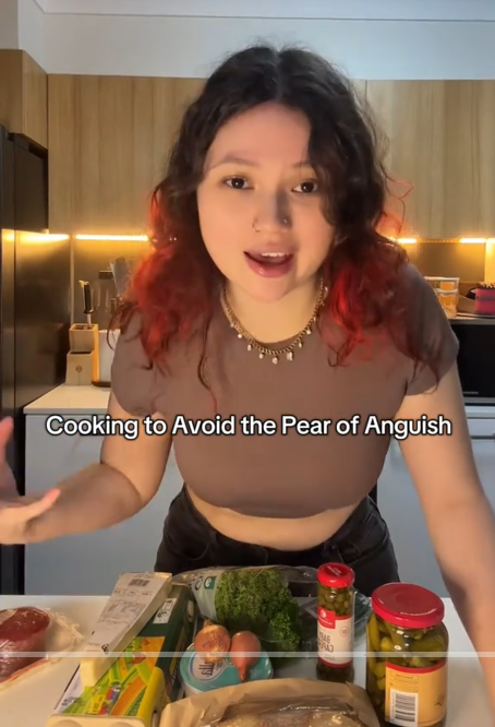 TikTok video with a woman speaking to the camera over ingredients with a caption reading "Cooking to Avoid the Pear of Anguish."